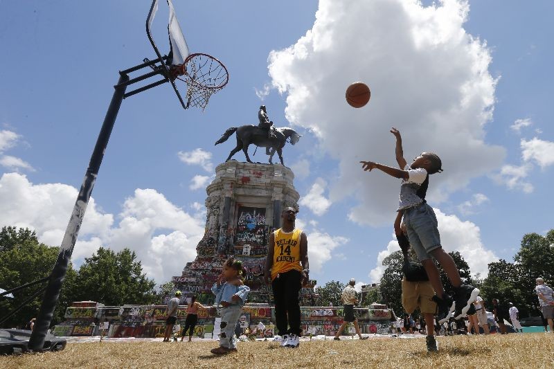 Isaiah Bowen, right, takes a shot as his dad, Garth Bowen, center, looks on at a basketball hoop in front of the statue of Confederate General Robert E. Lee on Monument Avenue  in Richmond, Va. A judge extended an injunction delaying the removal of the statue by the state. The statue had become a focal point for the Black Lives Matter movement in Richmond. (Photo by Steve Helber/AP Photo)